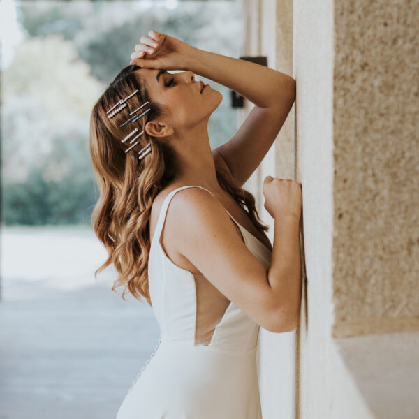 Mariée accoudée à un mur portant des bijoux de mariage dans sa coiffure. Ses cheveux sont lachés, attachés avec une multitude de barettes perlées et de barettes en cristal bleu.