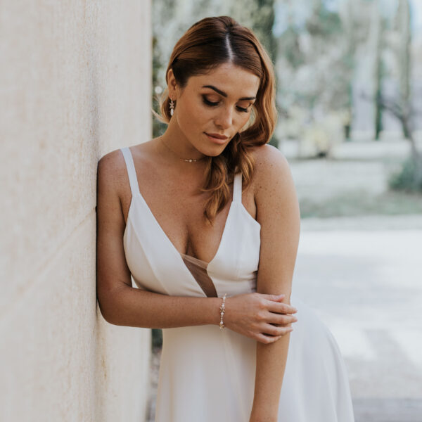 Jeune mariée portant ses bijoux de mariage. La parure se compose d'un collier simple et délicat avec de perles et du cristal de Swarovksi, des boucles d'oreilles avec gouttes et un bracelet alternant perles et cristal.