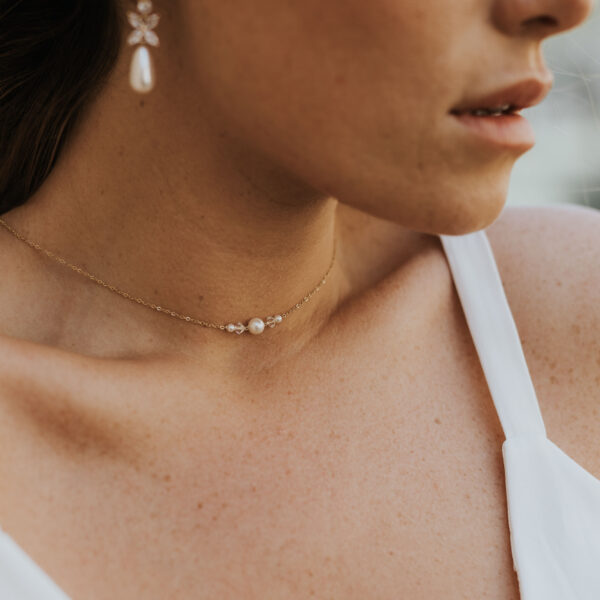 Jeune mariée portant ses bijoux de mariage. La parure se compose d'un collier simple et délicat avec de perles et du cristal de Swarovksi, et des boucles d'oreilles avec gouttes.
