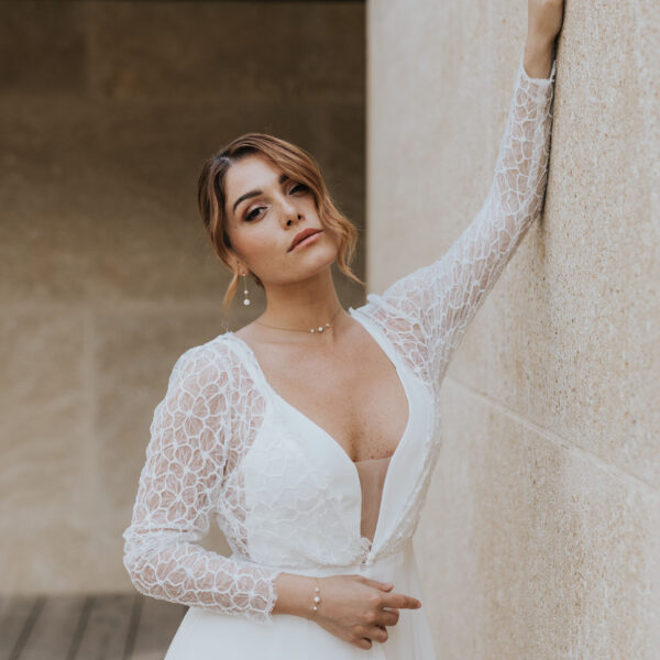Mariée portant des bijoux de mariage élégants et minimalistes en perles d'eau douc et porcelaine. Elle porte un collier ras de cou sur une fine chaîne, un bracelet et des boucles d'oreilles pendantes.