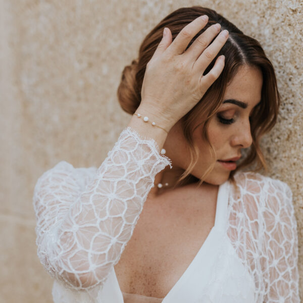 Mariée portant des bijoux de mariage élégants et minimalistes en perles d'eau douc et porcelaine. Elle porte un collier ras de cou sur une fine chaîne, un bracelet et des boucles d'oreilles pendantes.