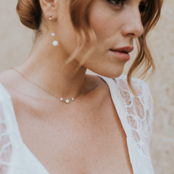 Mariée portant des bijoux de mariage élégants et minimalistes en perles d'eau douce et porcelaine. Son collier ras de cou et ses boucles d'oreilles pendantes sont montés sur une fine chaîne.